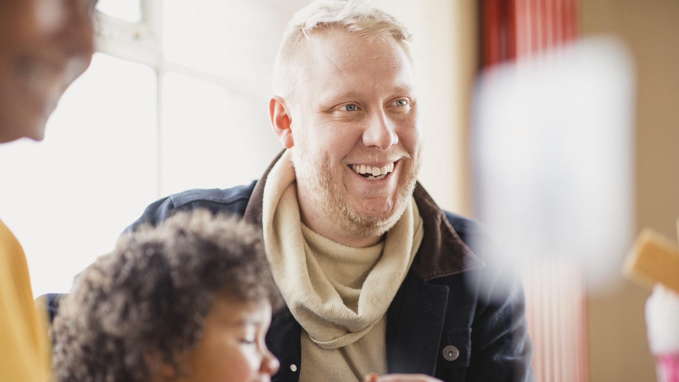 Personer i samtale rundt et bord i lyst miljø med naturlige smil og inkluderende stemning.