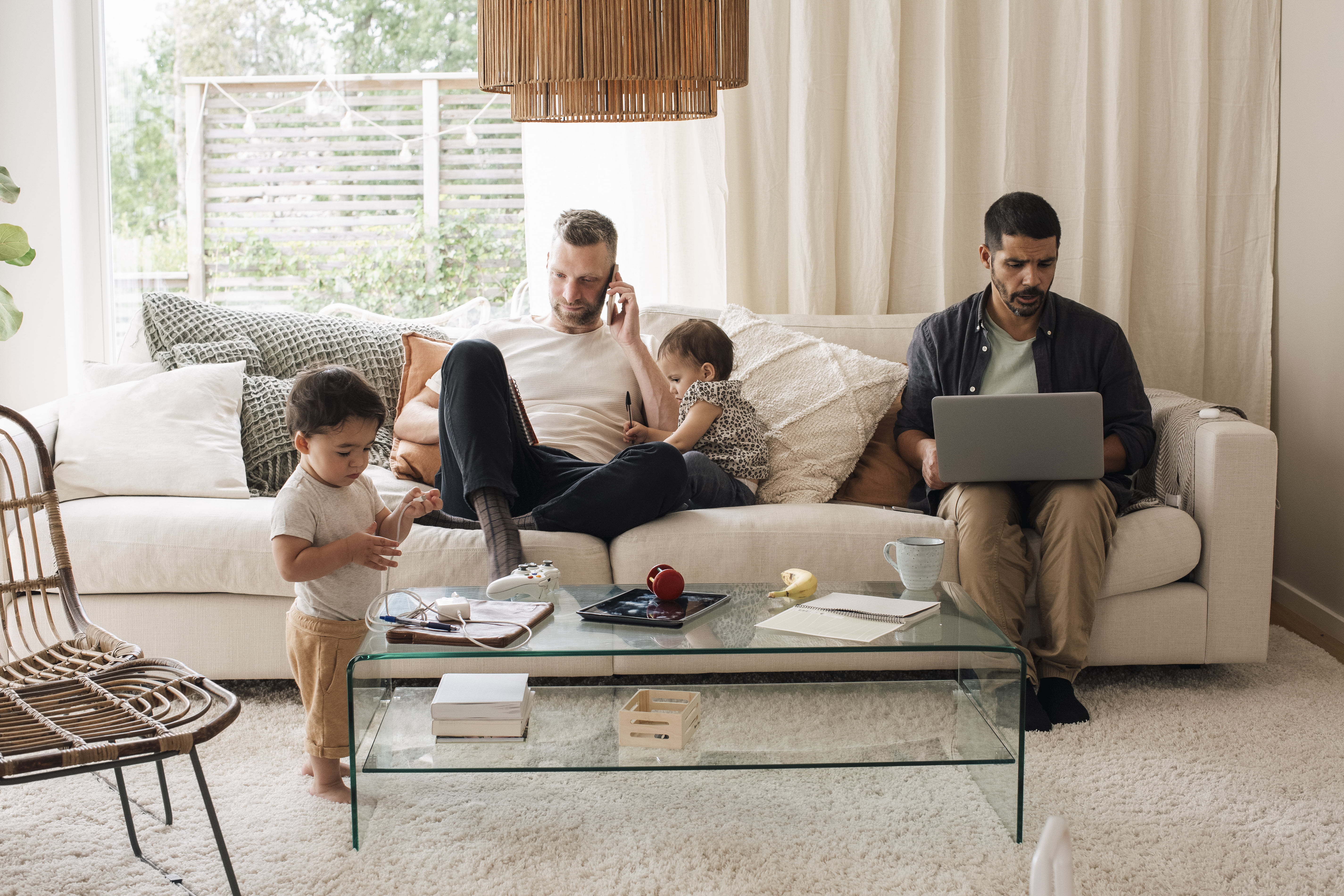 Par med to barn som sitter henslengt i sofa der en ser på PC og en er i mobilen.