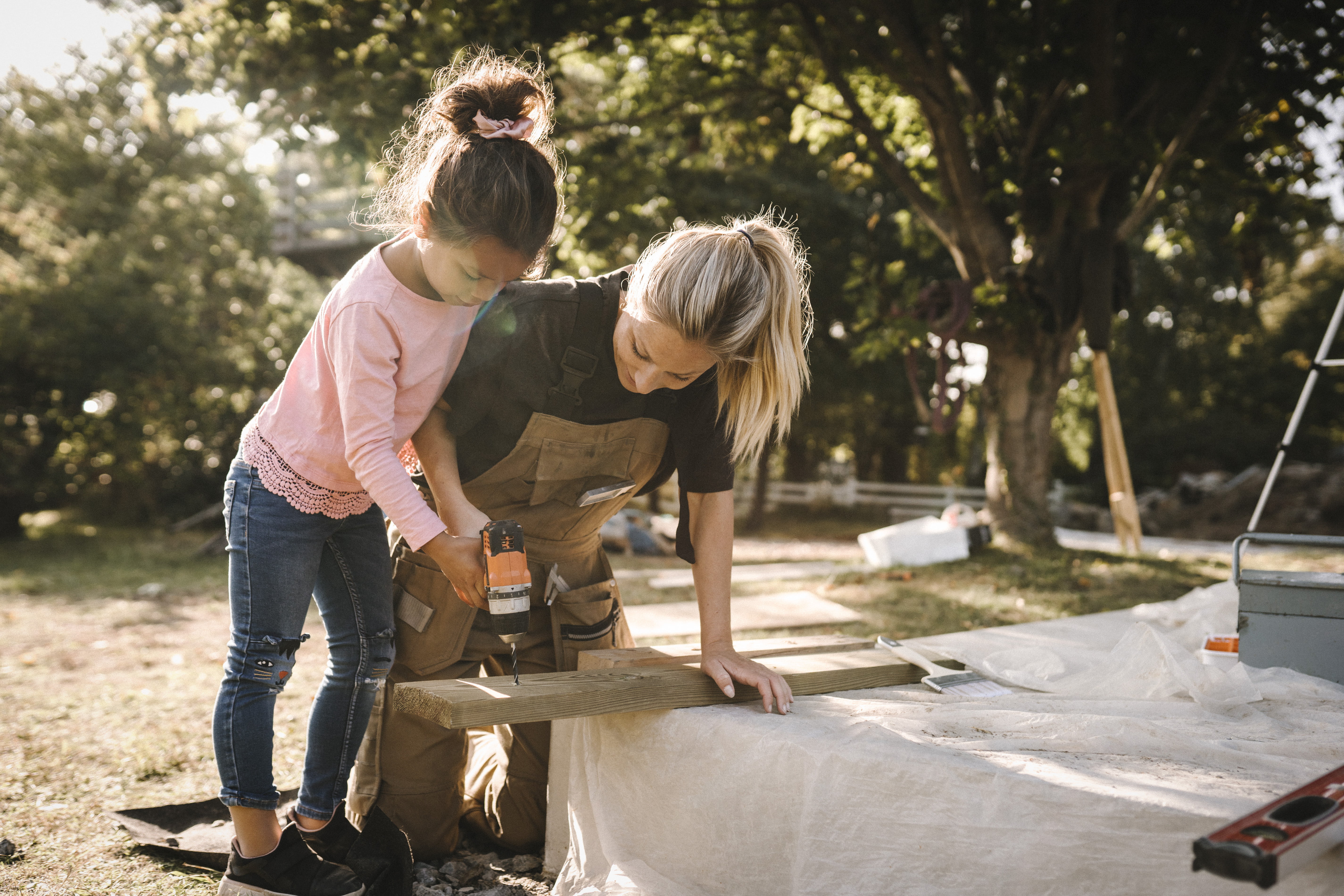 En mor som snekrer ute i hagen med datter ved siden av