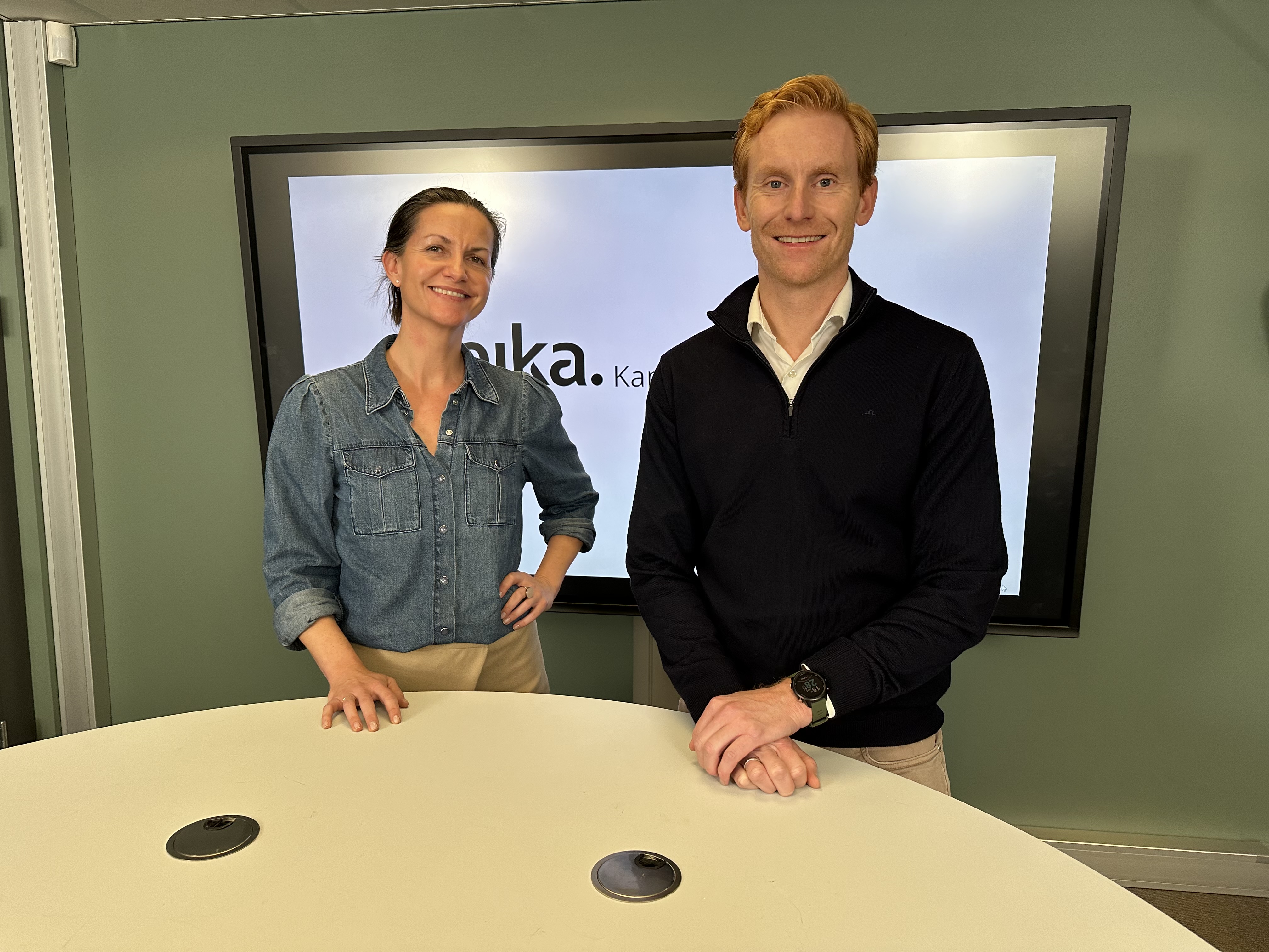 En blid Stine og Magnus står i et kontor i Eika