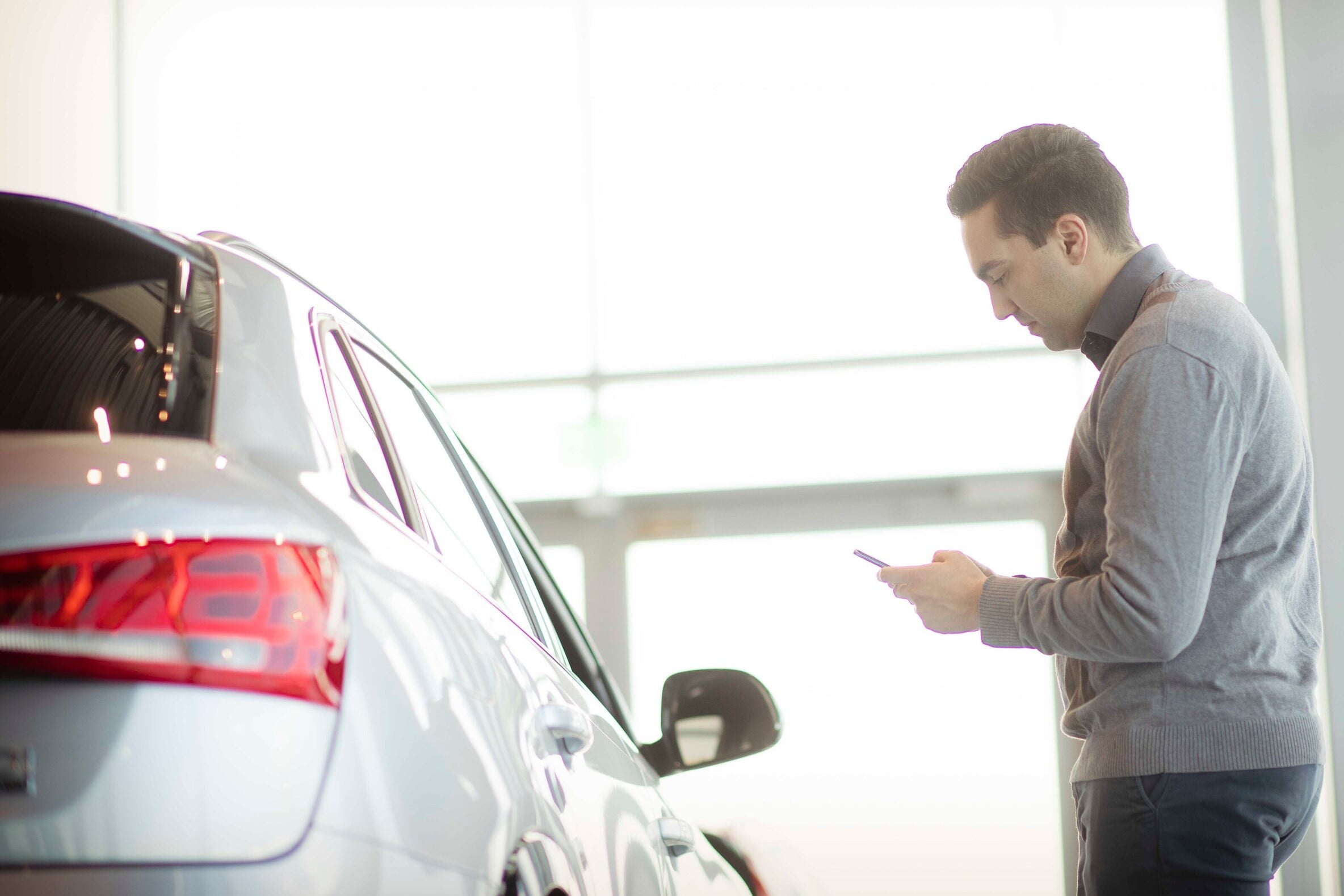 Ein mann står med mobilen i handa framfor ein bil