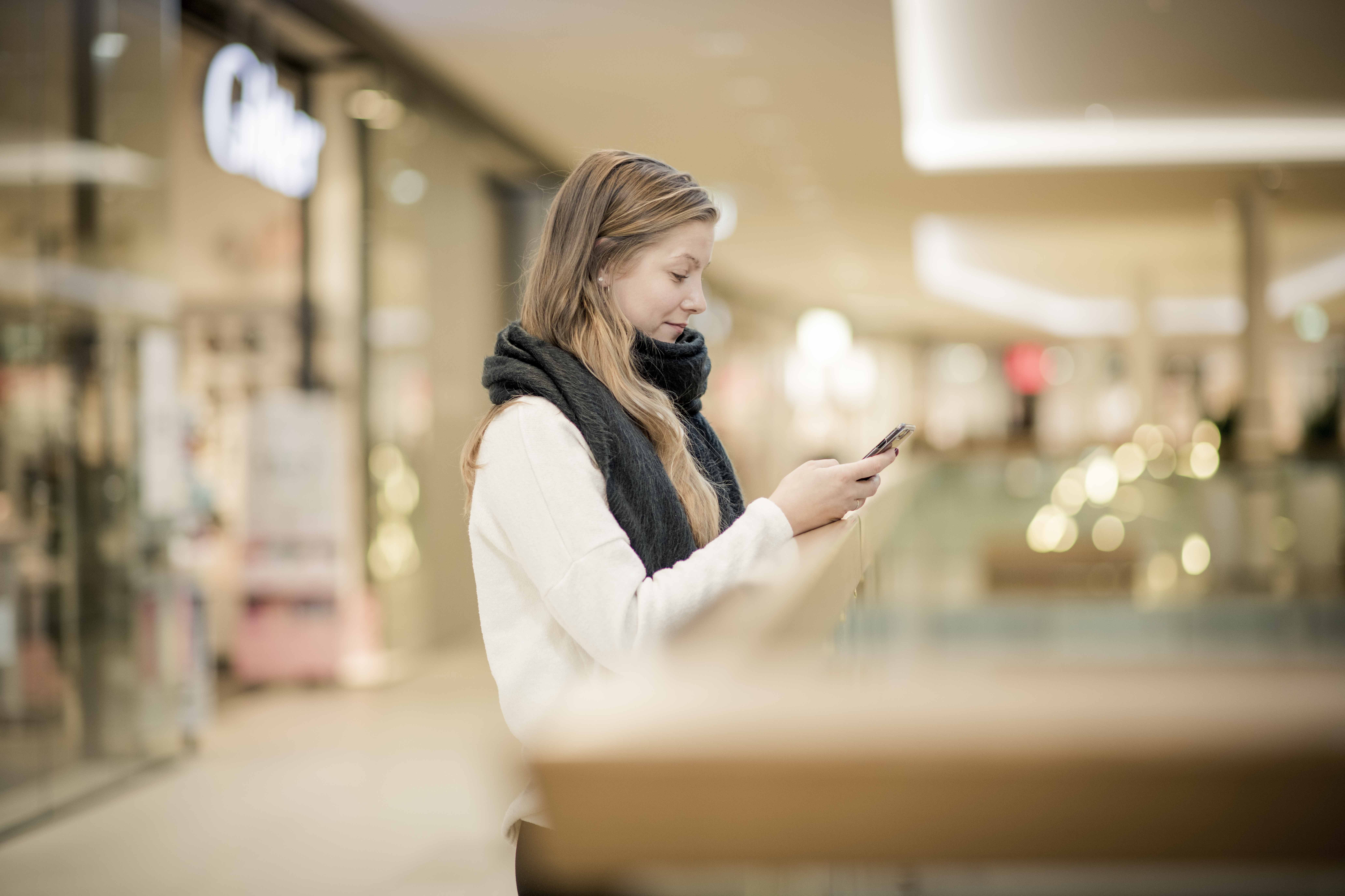 Bilde av ung dame på kjøpesenter som ser ned på mobilen