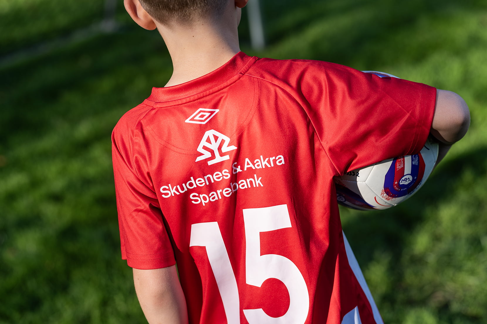 Nærbilde av barn i fotballdrakt med logoen til banken på ryggen.