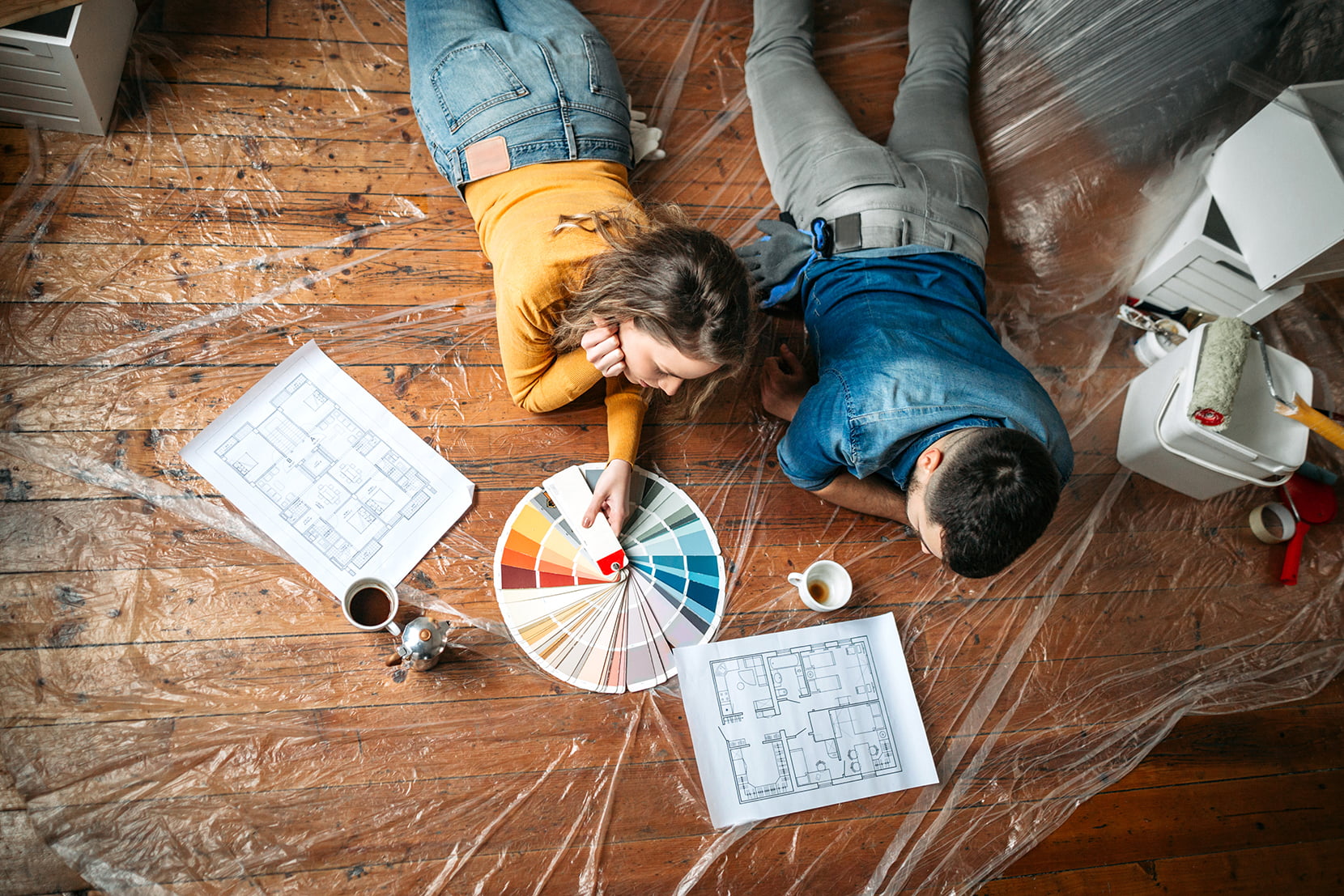 Mann og dame ligger på gulvet og planlegger oppussing med fargeprøver og plantegninger