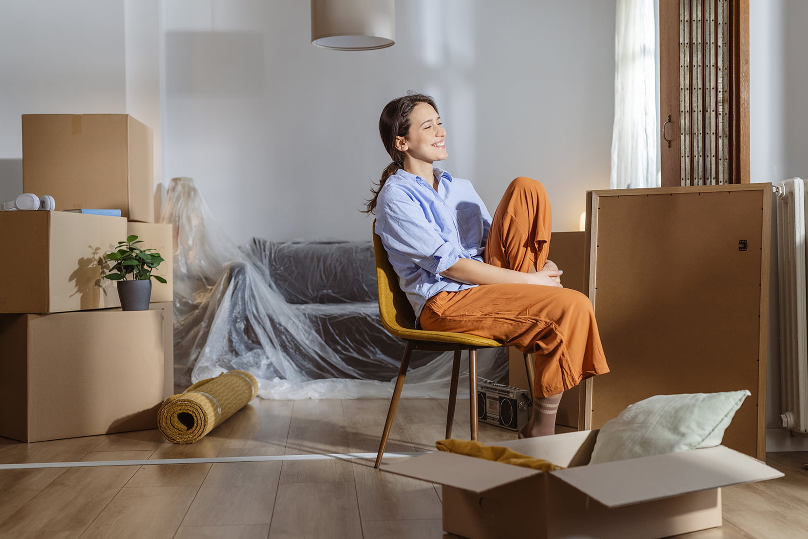 Kvinne som akkurat har flyttet inn i en bolig sitter blant esker og kikker ut av vinduet